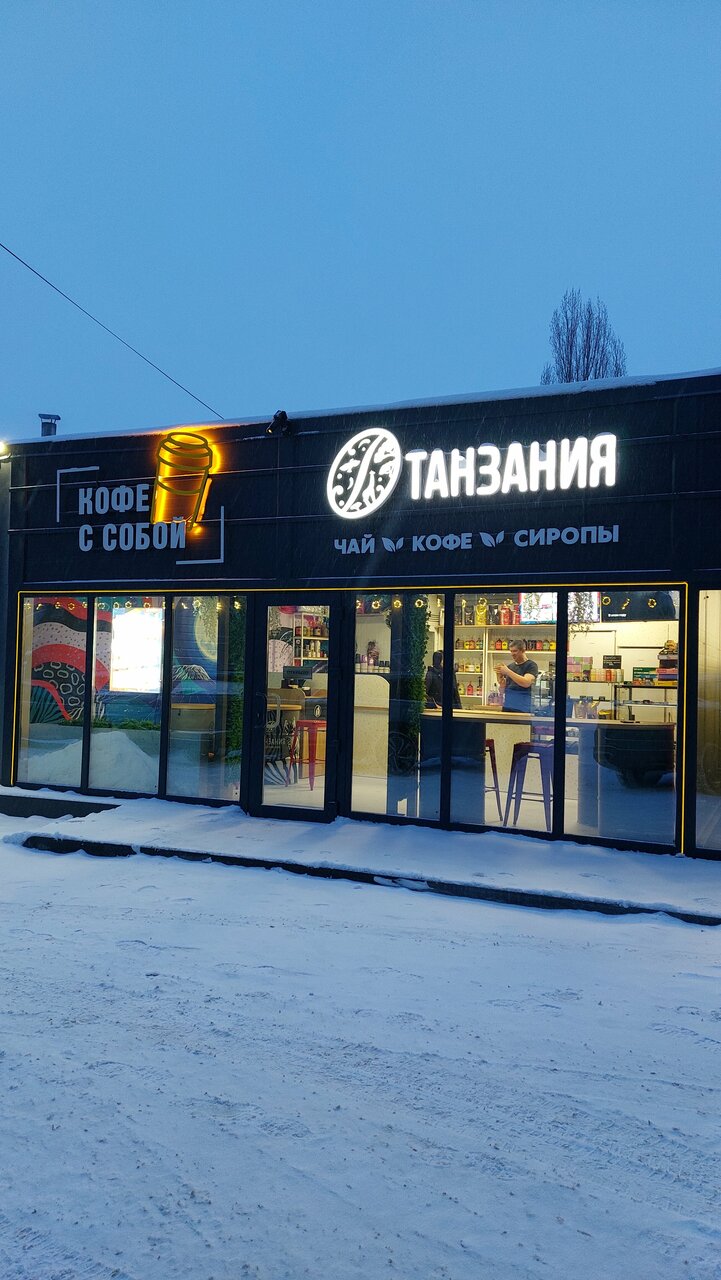 Фасад кофейни «Танзания» в Липецке вечером: чёрное здание с золотой вывеской и неоновым стаканом «Кофе с собой»